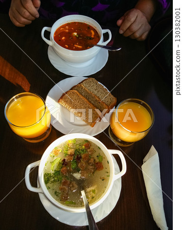 Mushroom Soup in a white bowls dark bread and fresh orange juice on rustic wooden table. Top view. Woman ready to have her lunch. Bone broth made from chicken in a white bowl with fresh vegetables 130382001