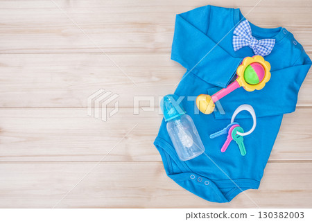Blue cotton bodysuit with baby toys. Baby boy clothes set isolated on wooden background, male child clothing. Infant wear and baby rattle with feeding bottle. Kid's care concept, copy space for text Blue cotton bodysuit with baby toys. Baby boy clothes set isolated on wooden background, male child clothing. Infant wear and baby rattle with feeding bottle. Kid's care concept, copy space for text 130382003