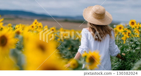 Woman in straw hat walking through vibrant sunflower field, enjoying nature's beauty and tranquility, surrounded by blooming flowers and greenery Woman in straw hat walking through vibrant sunflower field, enjoying nature's beauty and tranquility, surrounded by blooming flowers and greenery 130382024