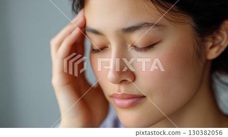 A young woman appears to be in discomfort, resting with eyes closed and a hand on her forehead 130382056