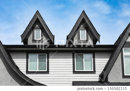 Facade of the house with nice window. Top of the wooden home. The roof of the house with nice window. Home exterior with blue sky on the background. Attic apartments background. House garret closeup 130382115