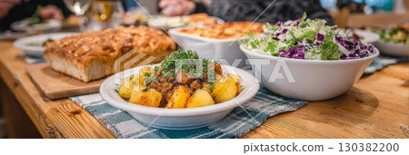 Delicious home-cooked meal featuring roasted potatoes, fresh salad, and bread on a rustic wooden table, showcasing culinary delights and dining experience 130382200