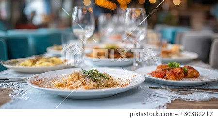 Elegant dining table set with various gourmet dishes and wine glasses, showcasing a vibrant culinary experience in a cozy restaurant atmosphere 130382217