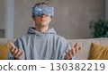 Young man wearing virtual reality headset is immersed in a cosmic experience, showcasing futuristic technology and digital exploration in a cozy setting 130382219