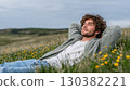 Young man relaxing in a field of wildflowers, enjoying nature and tranquility, with a serene expression and soft clouds in the sky 130382221