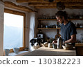 Man preparing food in rustic kitchen with dog watching, surrounded by handmade pottery and natural light, showcasing a cozy culinary atmosphere 130382223