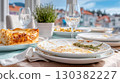 Delicious meal leftovers on elegant dining table with empty plates, wine glasses, and fresh herbs, showcasing a cozy dining atmosphere 130382227