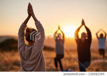 Wellness retreat at sunset with group practicing yoga in nature 130382364
