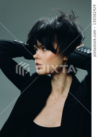 Stylish woman with short black hair in a black jacket posing against a dark background, showcasing modern fashion and confident expression. Stylish woman with short black hair in a black jacket posing against a dark background, showcasing modern fashion and confident expression. 130382424