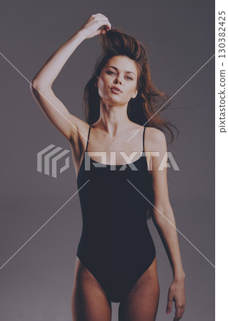 slender woman in black bodysuit posing against gray background with confident expression and natural makeup 130382425