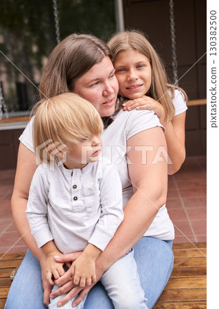 Caucasian woman with two children sharing a tender moment outdoors on a bench 130382500