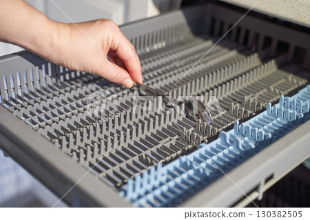 Female hand adjusting cutlery in dishwasher rack for efficient kitchen appliance Female hand adjusting cutlery in dishwasher rack for efficient kitchen appliance 130382505