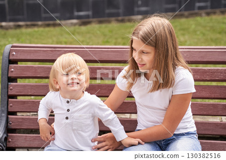 Caucasian child and teen girl sitting on a park bench smiling and enjoying sun 130382516