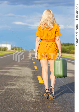 Blonde woman with a green retro suitcase walking on the highway. Blonde woman with a green retro suitcase walking on the highway. 130383867