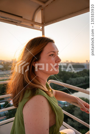 Woman in a green dress enjoys a sunset view from a high vantage point, with sunlight illuminating her hair Woman in a green dress enjoys a sunset view from a high vantage point, with sunlight illuminating her hair 130383910