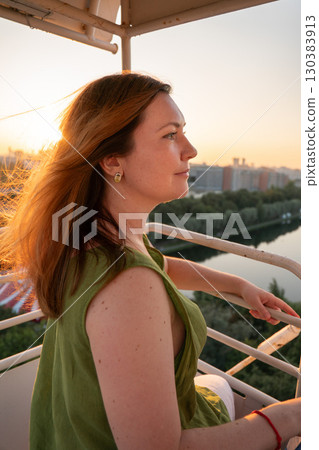 Woman in a green dress enjoys a sunset view from a high vantage point, with sunlight illuminating her hair 130383913
