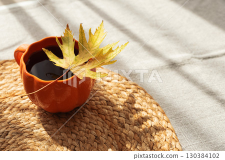 Pumpkin Mug with Coffee and Autumn Leaf on Woven Placemat 130384102