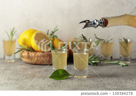 Italian liqueur Limoncello with fresh lemons and rosemary branches on a gray stone table. Italian liqueur Limoncello with fresh lemons and rosemary branches on a gray stone table. 130384278