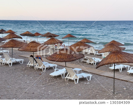 Beach with straw umbrellas and sun loungers by the sea. Summer vacation, relaxation and coastal leisure lifestyle. 130384309