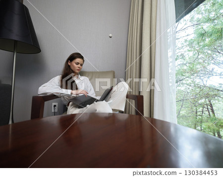 Thoughtful young woman in casual attire using laptop in a cozy indoor setting, surrounded by greenery and natural light, ideal for remote work concepts Thoughtful young woman in casual attire using laptop in a cozy indoor setting, surrounded by greenery and natural light, ideal for remote work concepts 130384453
