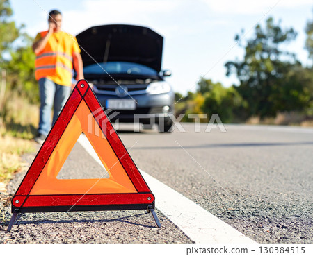 A man whose car has broken down on the road places a warning triangle and contacts road service 130384515