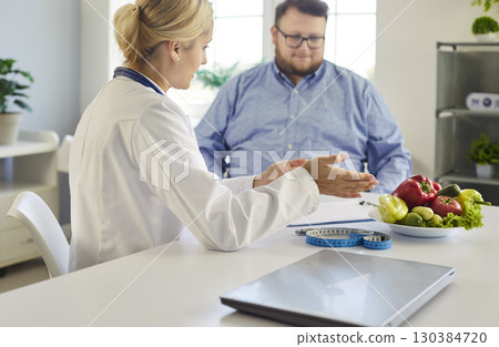 Nutritionist consulting overweight patient with vegetables, tape measure in clinic 130384720