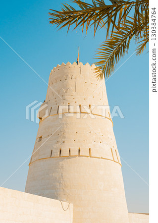 Stone arabic watchtower with waving United Arab Emirates National Flag in Al Jazirah Al Hamra haunted town in Ras Al Khaimah. High quality photo 130384764
