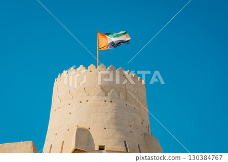 Stone arabic watchtower with waving United Arab Emirates National Flag in Al Jazirah Al Hamra haunted town in Ras Al Khaimah. High quality photo 130384767