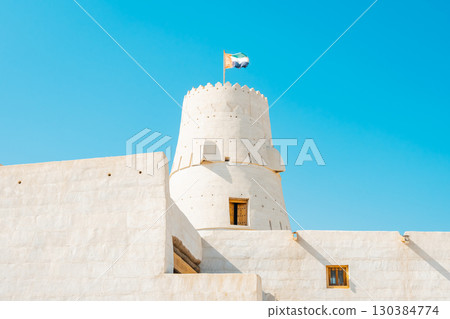Stone arabic watchtower with waving United Arab Emirates National Flag in Al Jazirah Al Hamra haunted town in Ras Al Khaimah. High quality photo 130384774