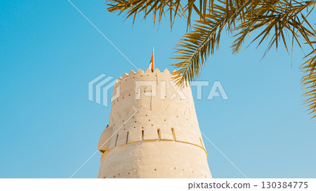 Stone arabic watchtower with waving United Arab Emirates National Flag in Al Jazirah Al Hamra haunted town in Ras Al Khaimah. High quality photo 130384775