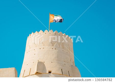 Stone arabic watchtower with waving United Arab Emirates National Flag in Al Jazirah Al Hamra haunted town in Ras Al Khaimah. High quality photo 130384782