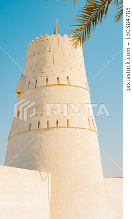 Stone arabic watchtower with waving United Arab Emirates National Flag in Al Jazirah Al Hamra haunted town in Ras Al Khaimah. High quality photo 130384783