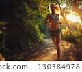 Fit female athlete running in sportswear along a scenic trail in the woods, enjoying an invigorating outdoor workout at sunset, captured with a dynamic motion blur effect 130384978