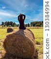 A woman is sitting on a hay bale in a field. 130384994