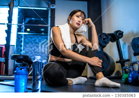 A woman taking a break and wiping sweat with a towel. A cool woman exercising at the gym. 130385063