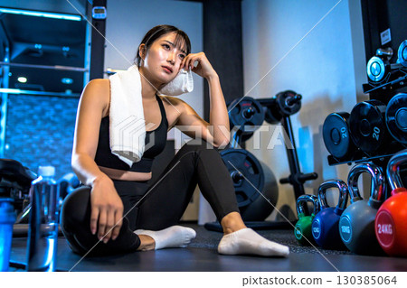A woman taking a break and wiping sweat with a towel. A cool woman exercising at the gym. A woman taking a break and wiping sweat with a towel. A cool woman exercising at the gym. 130385064