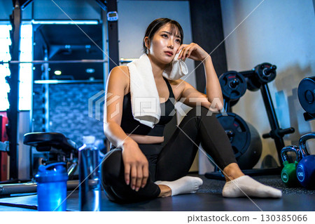 A woman taking a break and wiping sweat with a towel. A cool woman exercising at the gym. A woman taking a break and wiping sweat with a towel. A cool woman exercising at the gym. 130385066