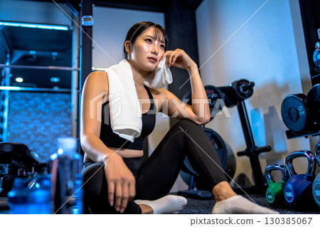A woman taking a break and wiping sweat with a towel. A cool woman exercising at the gym. 130385067