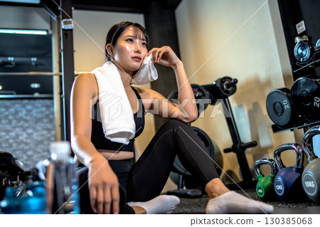 A woman taking a break and wiping sweat with a towel. A cool woman exercising at the gym. 130385068