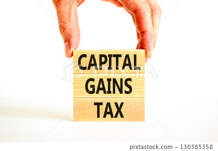 Capital gains tax symbol. Concept words Capital gains tax on beautiful wooden block. Businessman's hand. Beautiful white background. Business and capital gains tax concept. Copy space. 130385358