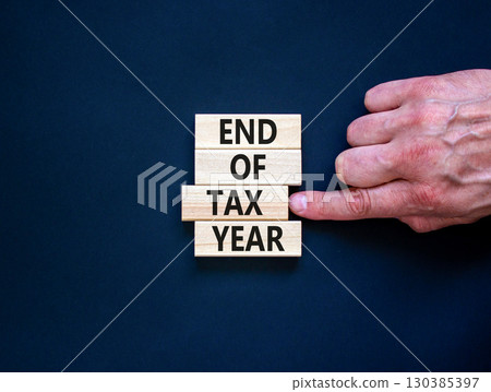 End of tax year symbol. Concept words phrase End of tax year on beautiful wooden blocks. Beautiful black paper background. Businessman's hand. Business End of tax year concept. Copy space. 130385397