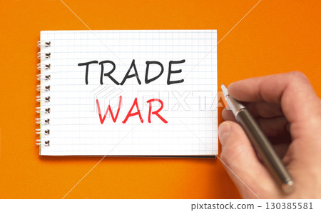 Trade war symbol. Concept word Trade war on beautiful white note. Businessman's hand with pen. Beautiful orange paper background. Business trade war concept. Copy space. Trade war symbol. Concept word Trade war on beautiful white note. Businessman's hand with pen. Beautiful orange paper background. Business trade war concept. Copy space. 130385581