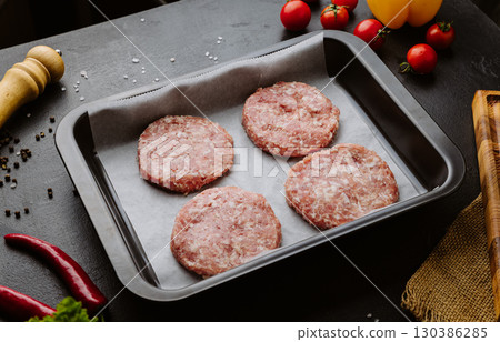 Fresh raw burger cutlets with spices and vegetables on black background, ready for cooking 130386285