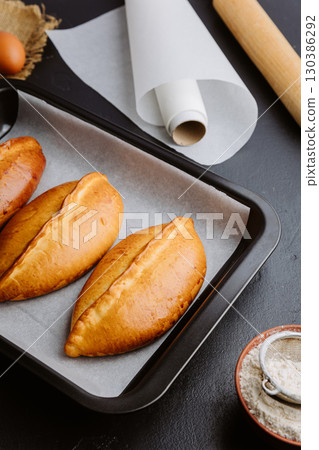 Freshly baked pies in baking tray, traditional homemade pastry with golden crust. Ukrainian piroshki 130386292
