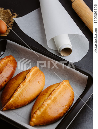 Golden homemade pies in baking tray, rustic kitchen scene with rolling pin and eggs 130386306