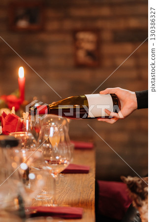 Pouring rose wine into glass at festive dinner with flowers and candlelight ambiance 130386327