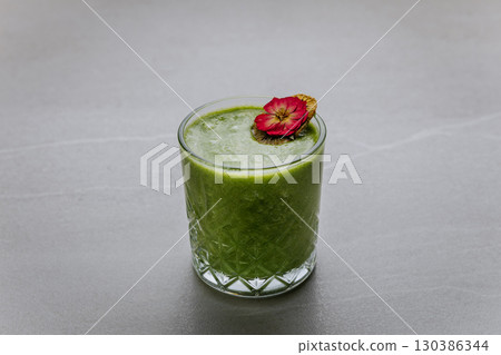 Healthy green smoothie with dried kiwi and edible flower in glass on gray stone background 130386344