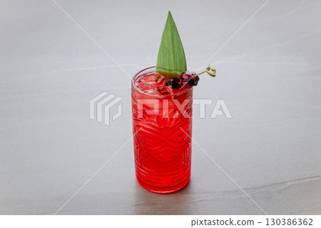 Red tropical cocktail with ice, berries and leaf garnish on light background 130386362