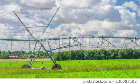Irrigation System Operates in a Lush Green Field Beneath a Clear Blue Sky Filled with Clouds 130387108