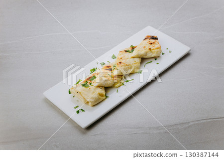 Grilled lavash rolls with melted cheese and herbs on a white ceramic plate 130387144
